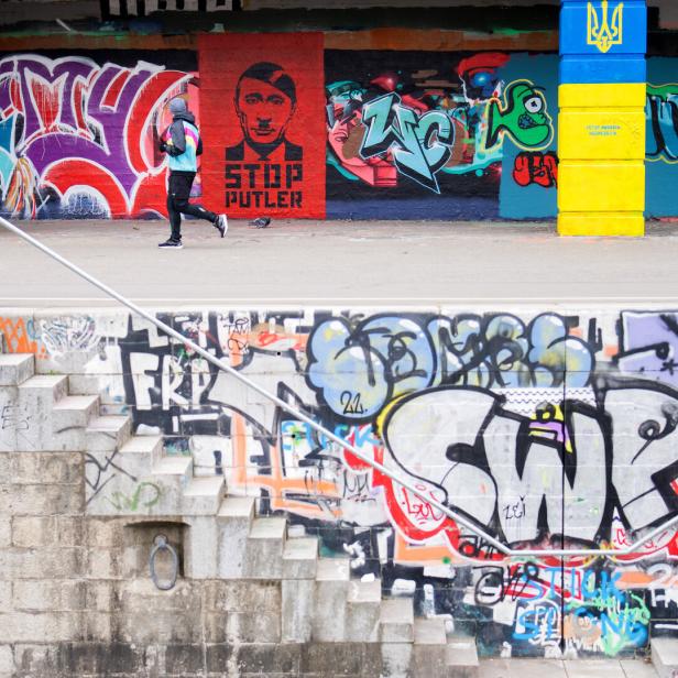 Eine Person joggt vor einer Wand mit Graffiti und einem Anti-Putin-Porträt.