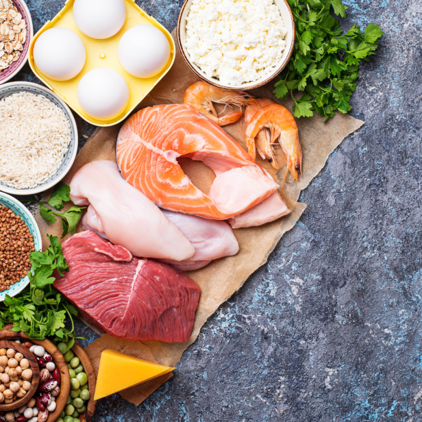 Verschiedene proteinreiche Lebensmittel wie Fleisch, Fisch, Eier und Hülsenfrüchte auf einem Tisch angerichtet.