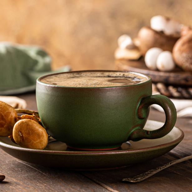 Eine Tasse Pilzkaffee steht auf einem Holztisch, umgeben von Pilzen und Kaffeebohnen.