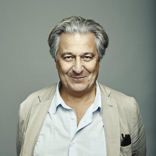 Ein lächelnder Mann mit grauem Haar trägt ein helles Sakko und ein hellblaues Hemd.