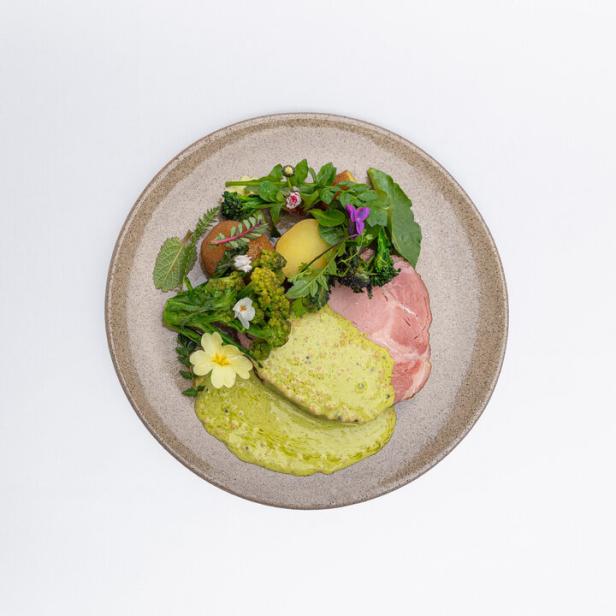 Mangalitza-Schinken mit Kartoffeln, Gemüse und grüner Soße auf einem Teller.
