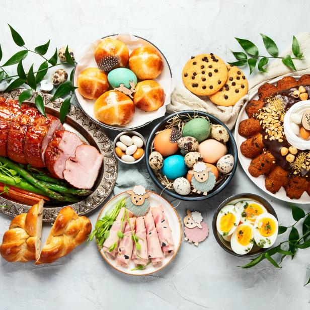 Ein festliches Ostermahl mit Schinken, Eiern, Gebäck und Osterdekorationen auf einem Tisch.