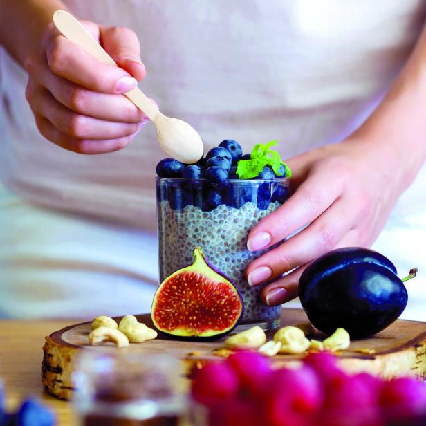 Eine Person bereitet ein Chia-Pudding mit Blaubeeren, Feigen und Pflaumen zu.