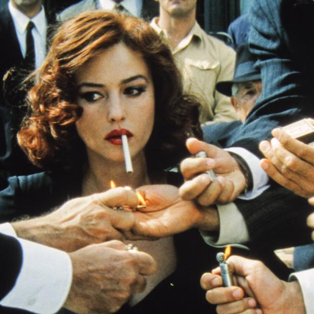 Monica Bellucci mit Zigarette im Mund, umringt von Männern, die ihr Feuer geben.