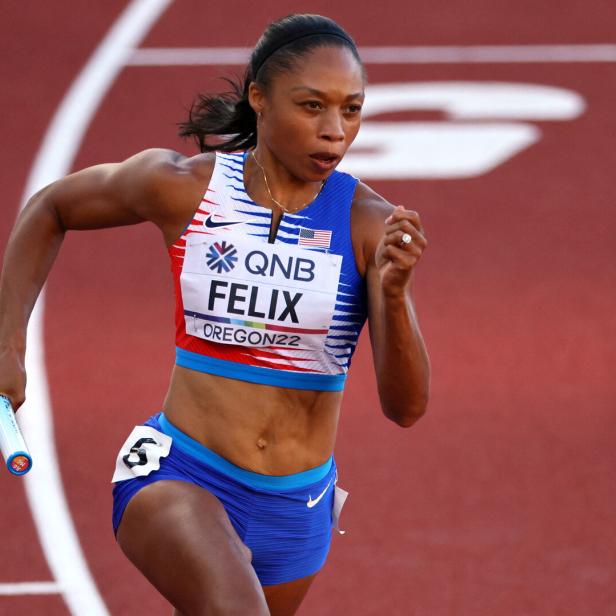 Allyson Felix läuft mit einem Staffelstab auf einer roten Laufbahn.