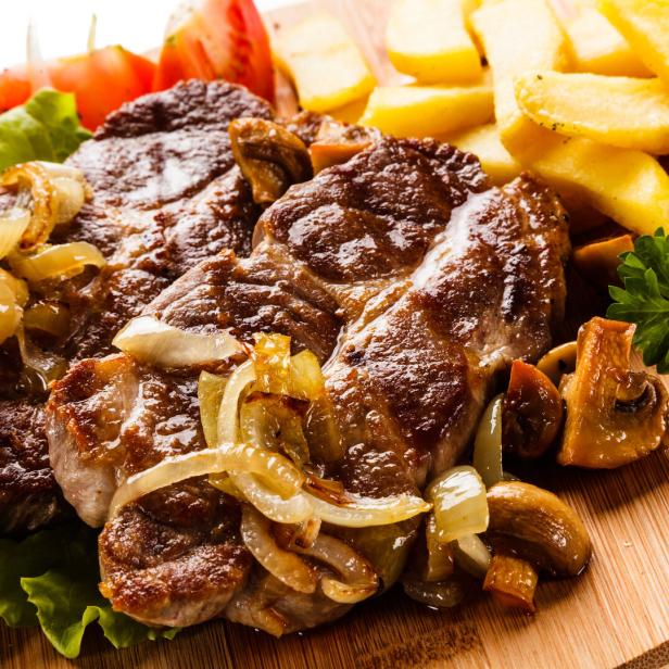 Ein Teller mit Steak, Bratkartoffeln und Zwiebeln garniert mit Salat und Tomaten.