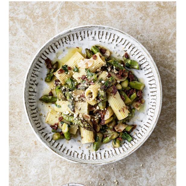 Ein Teller Rigatoni mit Spargel, sonnengetrockneten Tomaten und gerösteten Nüssen.