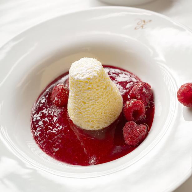 Ein Dessert mit Himbeersauce, frischen Himbeeren und einer kleinen, puderzuckerbestäubten Kuppel.