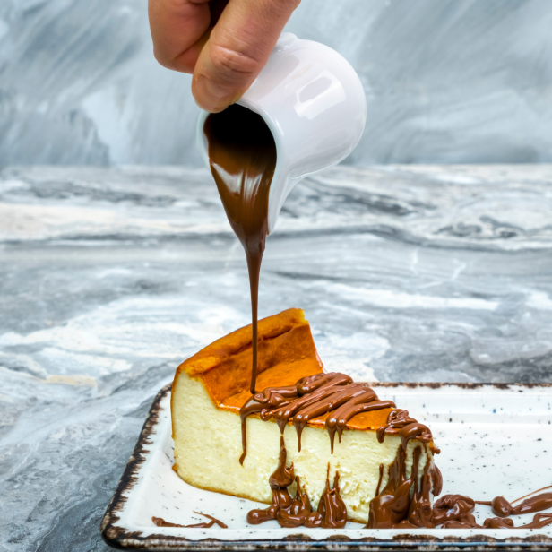 Ein Stück Käsekuchen wird mit Schokoladensoße übergossen.