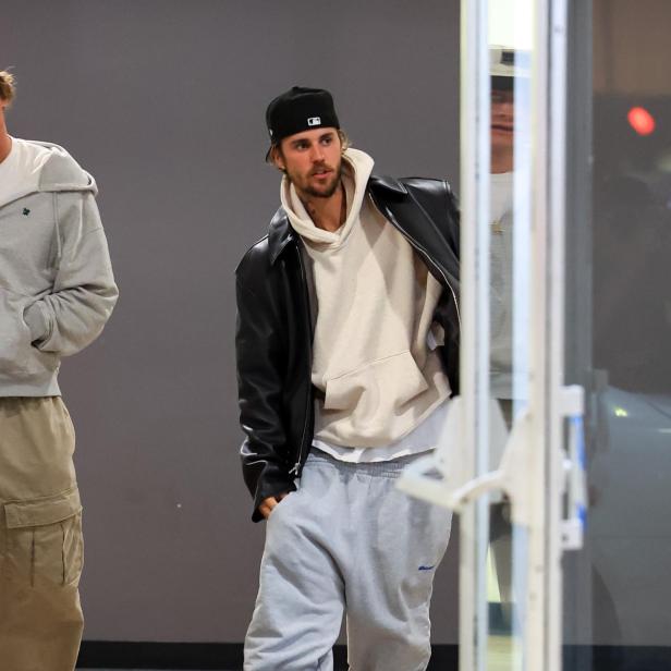 Justin Bieber trägt eine schwarze Jacke, einen Hoodie und Hausschuhe.