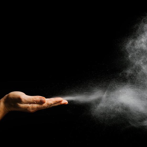 Eine Hand wirft eine Wolke aus weißem Pulver in die Luft.