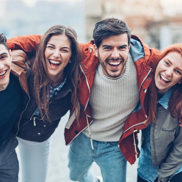Vier lachende Freunde umarmen sich im Freien.