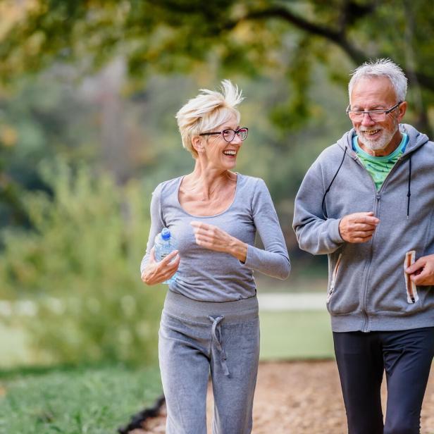 Frau und Mann joggen lachend im Park.