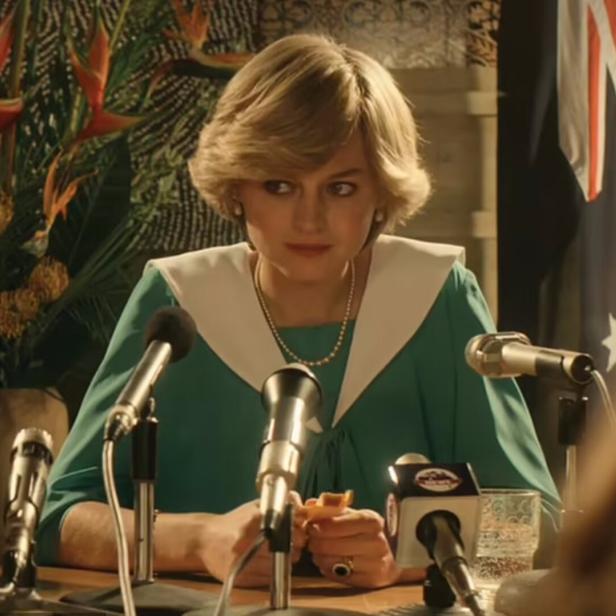 Eine Frau im grünen Kleid steht vor Mikrofonen und einer australischen Flagge.