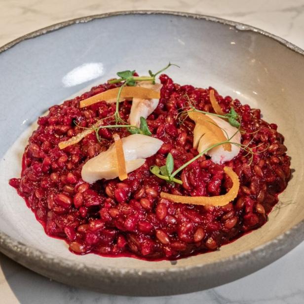 Ein Teller mit rotem Risotto, garniert mit Birnenstücken und Orangenzesten.