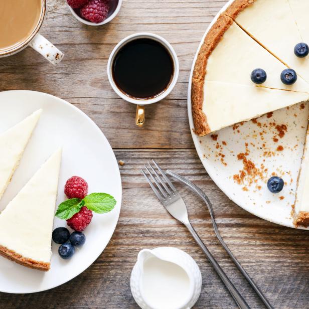 Ein Käsekuchen mit Beeren und Minze wird zusammen mit Kaffee auf einem Holztisch serviert.