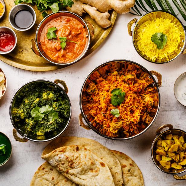 Verschiedene indische Gerichte, darunter Curry, Reis und Brot, sind auf einem Tisch angerichtet.