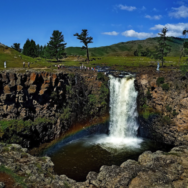 Ein Wasserfall stürzt über eine Klippe, am Fuße des Wasserfalls ist ein Regenbogen zu sehen.