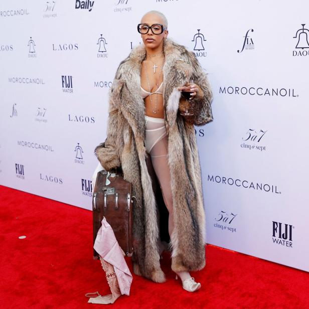 Doja Cat mit Pelzmantel und Koffer auf einem roten Teppich.