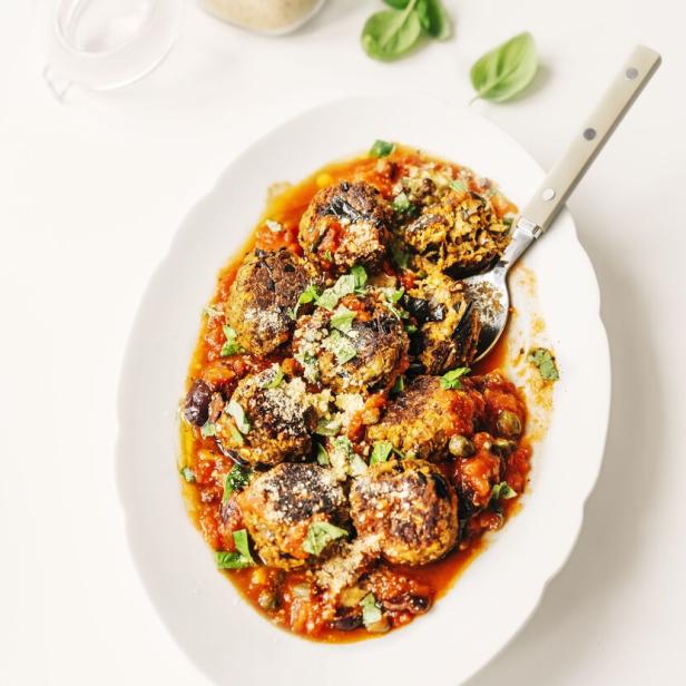 Auf einer Platte liegen Auberginen-Bällchen in Tomatensauce, garniert mit Basilikum und Parmesan.