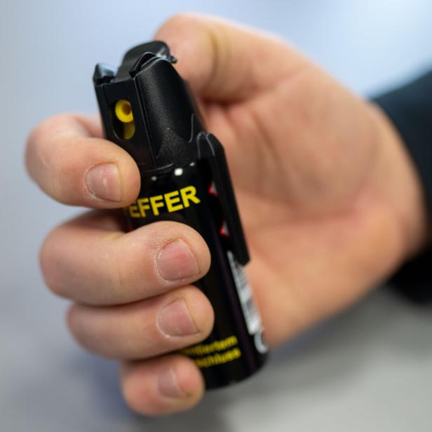 Eine Hand hält eine schwarze Pfefferspraydose mit gelber Aufschrift und bereitet sich auf die Benutzung vor.