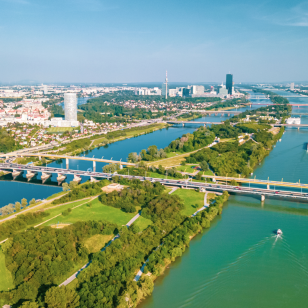 Luftaufnahme von Wien mit der Donau, mehreren Brücken und der Skyline im Hintergrund.