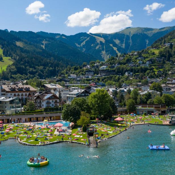 Blick auf Zell am See mit Badegästen am Ufer und Bergen im Hintergrund.