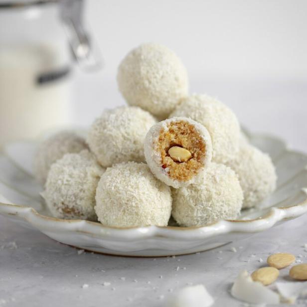 Ein Teller mit Kokosnussbällchen, von denen eines halbiert ist und eine Mandel zeigt.