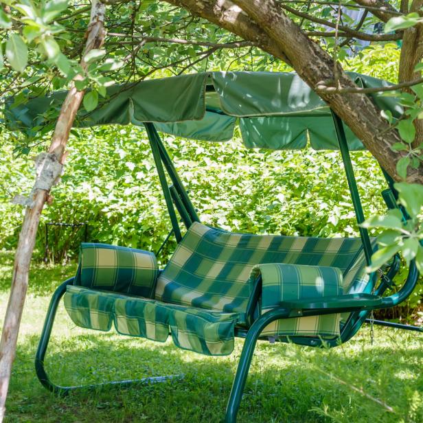 Eine grüne Gartenschaukel steht im Schatten eines Baumes.