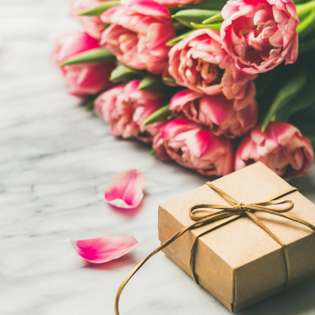 Ein Geschenk liegt neben einem Strauß rosa Tulpen auf einem Marmortisch.