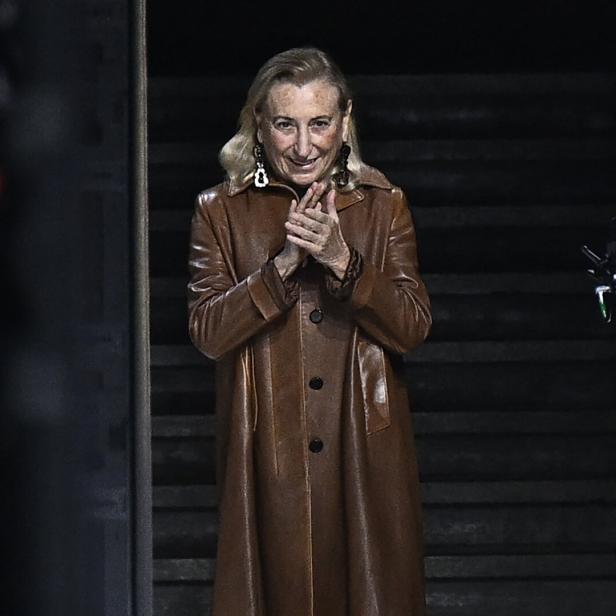 Miuccia Prada in einem braunen Ledermantel klatscht in die Hände.