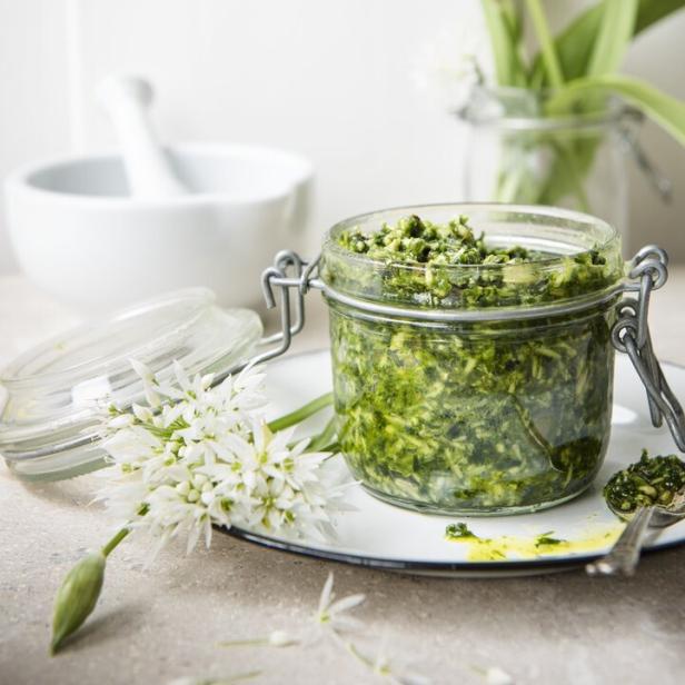 Ein Glas Bärlauchpesto steht auf einem Teller, dekoriert mit Bärlauchblüten.