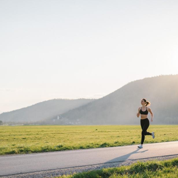 Eine Frau joggt auf einer Landstraße vor einer grünen Wiese und Bergen.