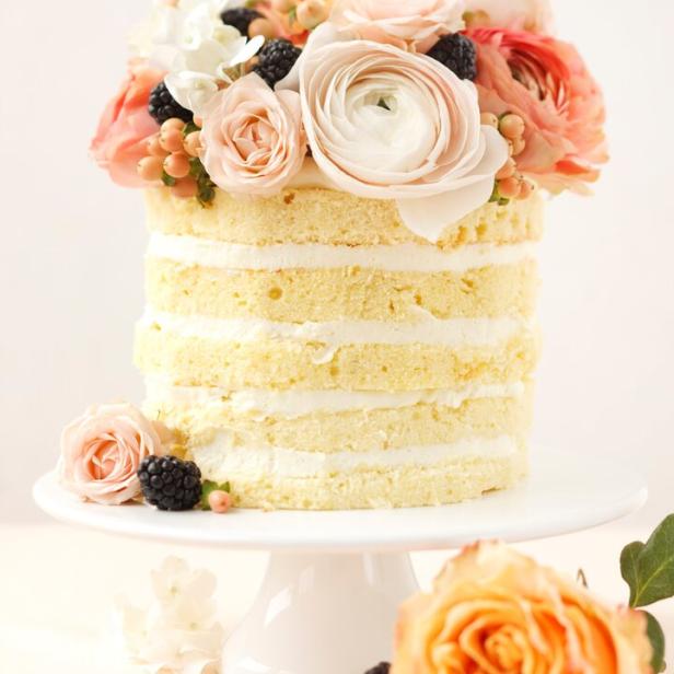 Ein Naked Cake mit Blumen und Brombeeren auf einem weißen Teller.