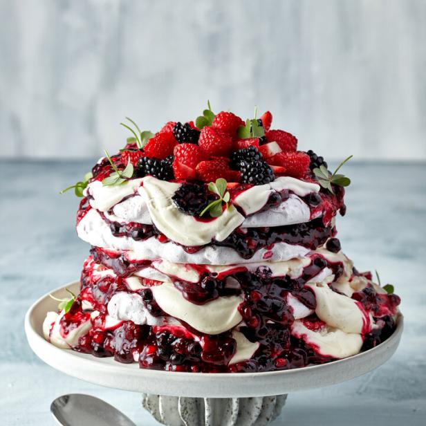 Eine mehrschichtige Pavlova-Torte mit Beeren und Creme, serviert auf einem Tortenständer.