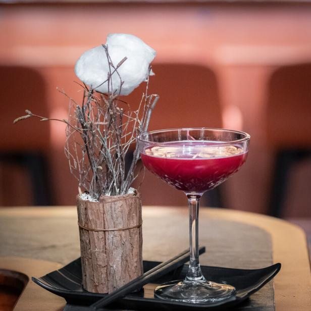 Ein Waldmeister-Gin-Cocktail neben einer Dekoration mit Baumwolle und Ästen.
