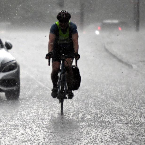 Ein Radfahrer fährt bei starkem Regen auf einer nassen Straße neben einem Auto.