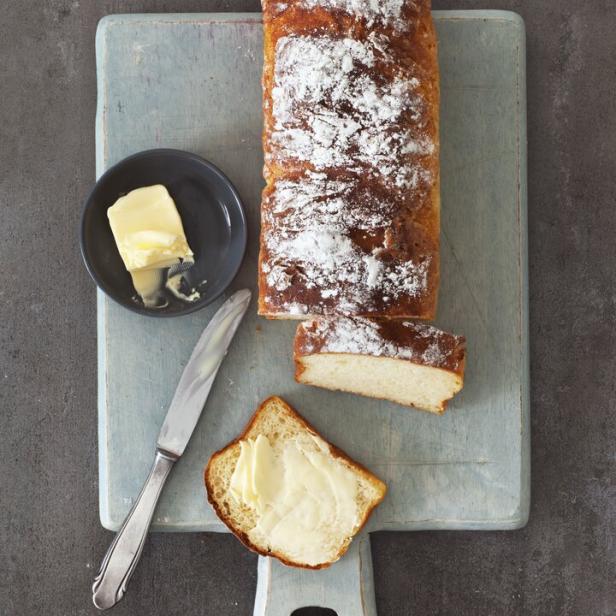 Ein Topfenbrot mit Puderzucker, Butter und einem Messer auf einem Schneidebrett.