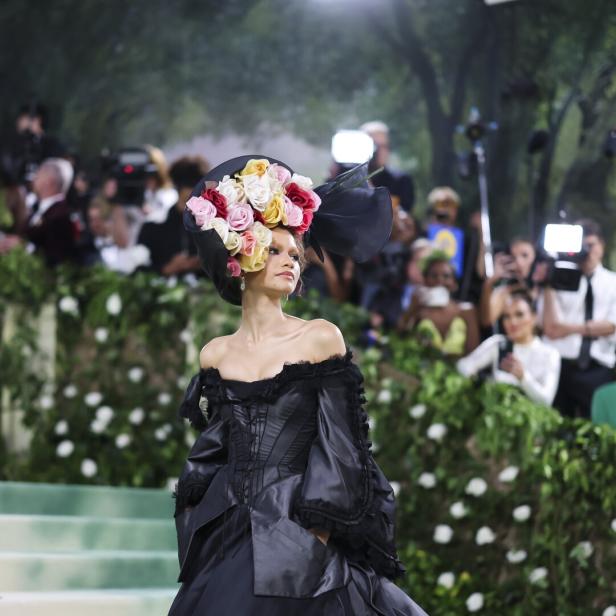 Ein Model mit einem schwarzen Kleid und einem Hut mit Blumen auf einer Treppe.