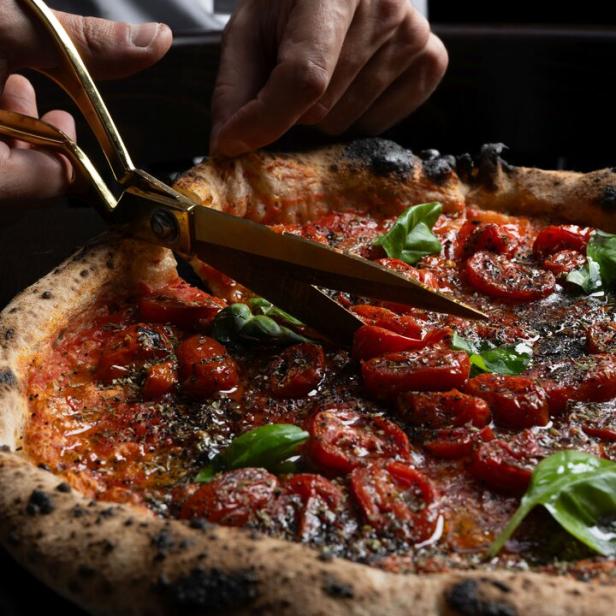 Eine Pizza Marinara wird mit einer goldenen Schere geschnitten.