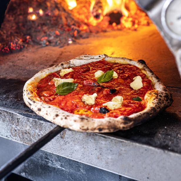 Eine Pizza mit Tomatensoße, Mozzarella und Basilikum wird in einem Holzofen gebacken.