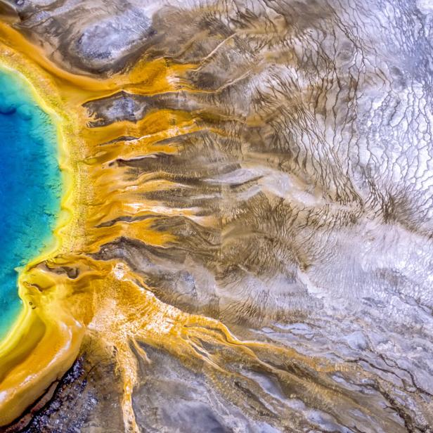 Luftaufnahme einer Thermalquelle mit blauem Wasser und gelben Ablagerungen.