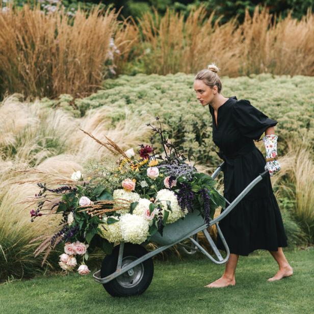 Eine Frau schiebt eine Schubkarre voller Blumen durch einen Garten.