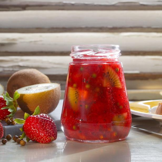 Ein Glas Erdbeer-Kiwi-Marmelade steht auf einem Tisch mit frischen Erdbeeren und Kiwis.