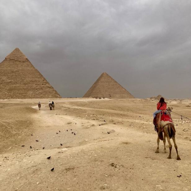 Eine Frau reitet auf einem Kamel vor den Pyramiden von Gizeh in Ägypten.