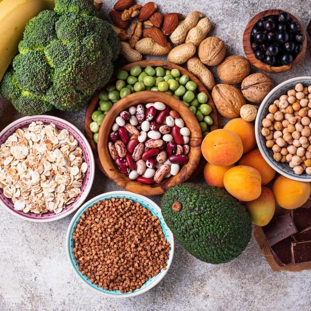 Verschiedene gesunde Lebensmittel wie Obst, Gemüse, Hülsenfrüchte und Nüsse sind auf einer Fläche angeordnet.