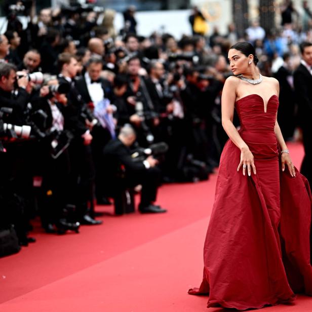 Eine Frau in einem roten Kleid posiert auf dem roten Teppich vor einer Menschenmenge.