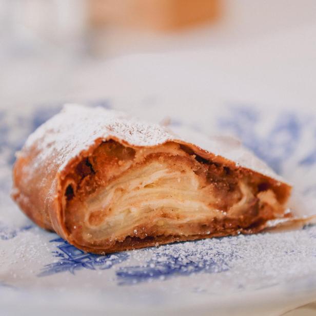 Ein Stück Apfelstrudel auf einem blau-weiß gemusterten Teller, mit Puderzucker bestäubt.