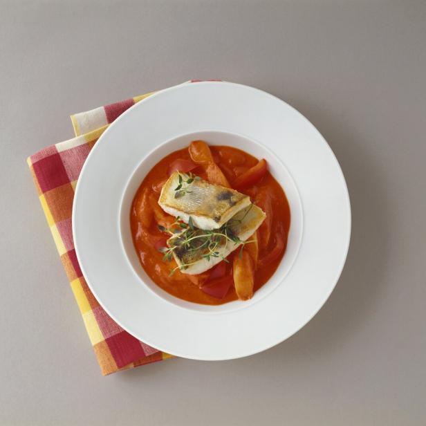Ein Teller mit Fischfilet in Tomatensoße, garniert mit Thymian, auf einem karierten Tuch.