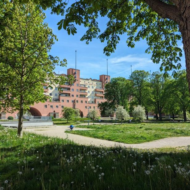 Der Karl-Marx-Hof, ein bekannter Wiener Gemeindebau, gesehen durch Bäume und eine Wiese.